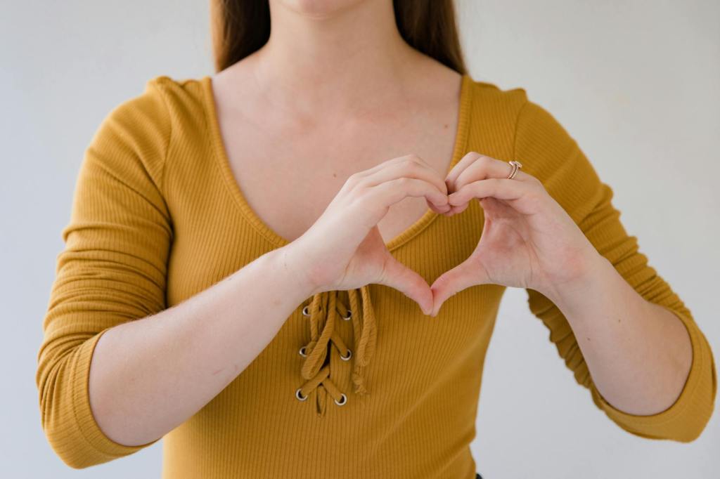 close up on woman in yellow blouse showing heart sign